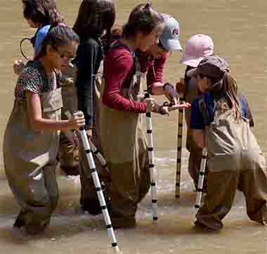 Christy Wall, (in grey hat) director of science and education with the New Mexico Wildlife Center, shows students some of the animals and rocks she found on the riverbed, Sept. 6, 2017.